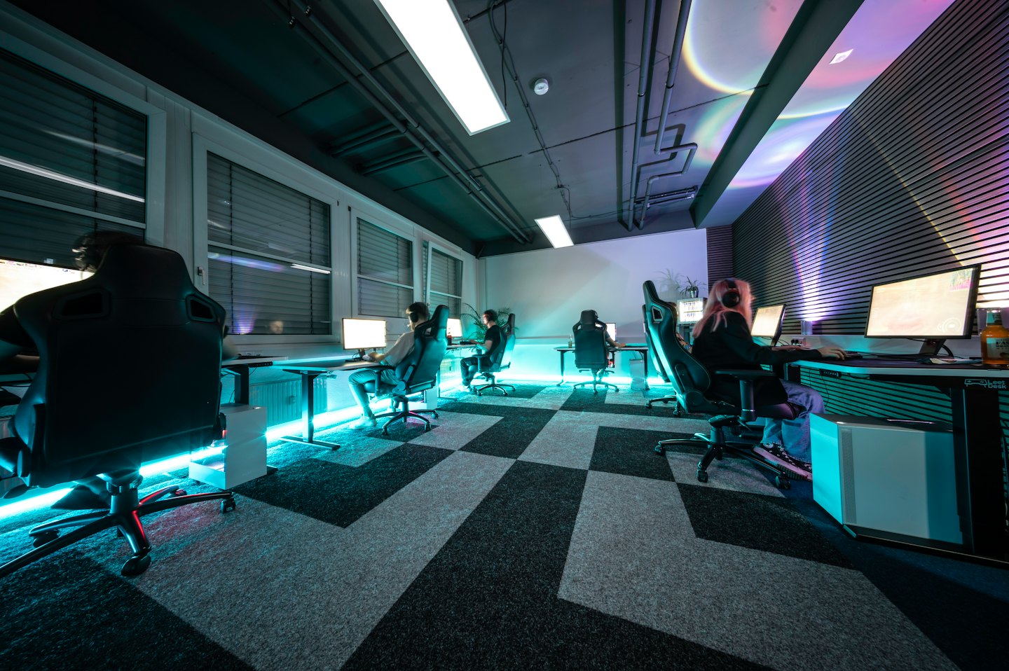 Cuatro adultos jugando intensamente en una moderna arena de esports con poca luz.
