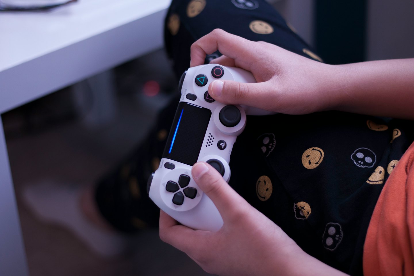 Manos sujetando un mando de videojuegos blanco con luz azul.