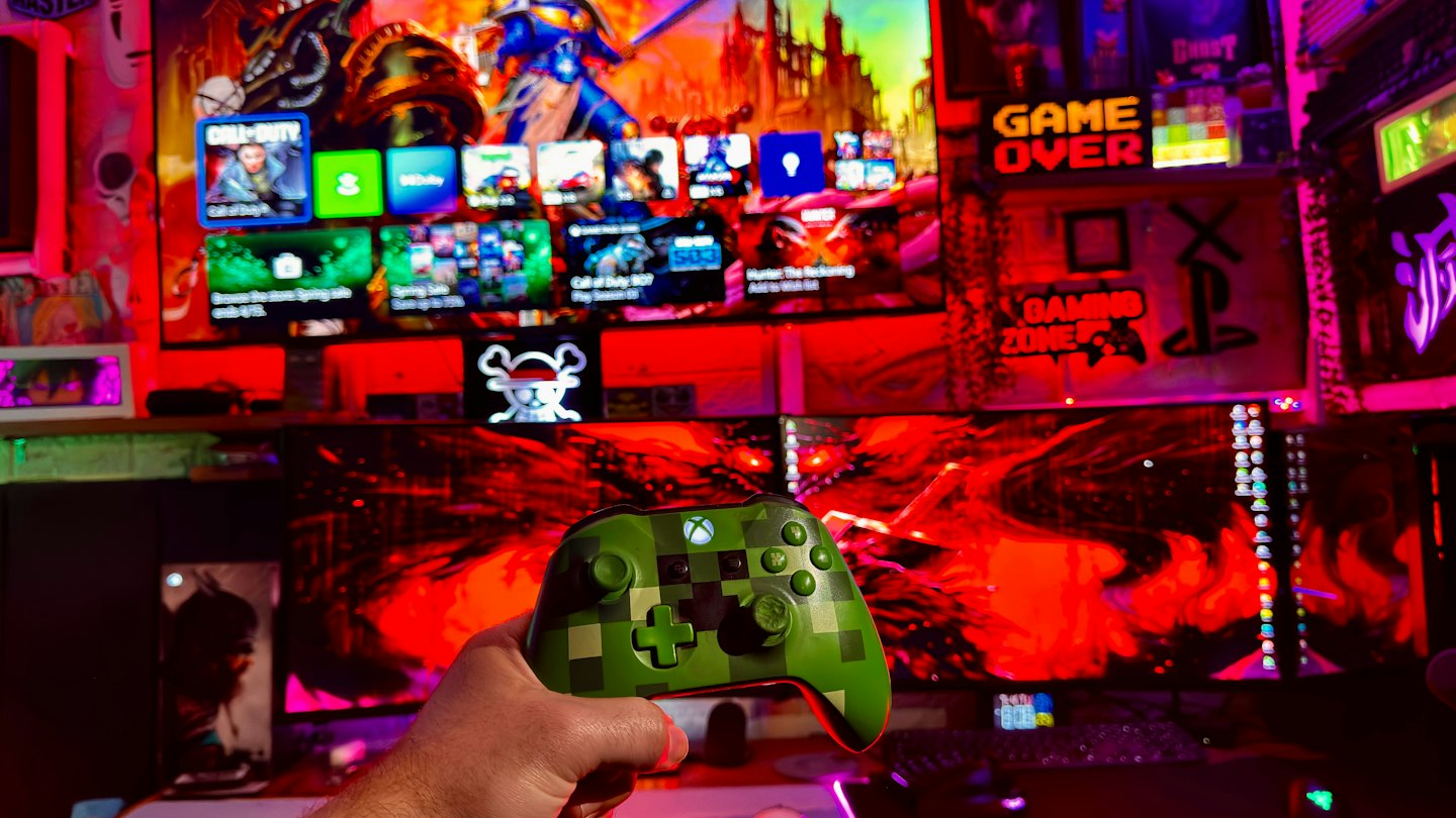 Mano sujetando un mando verde de Xbox con pantallas de videojuegos.